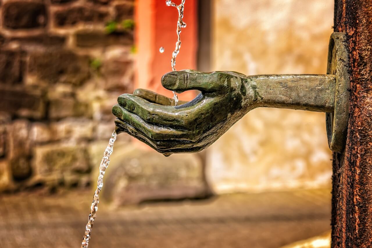 Bild på fontän som fångar upp rent vatten i händerna.